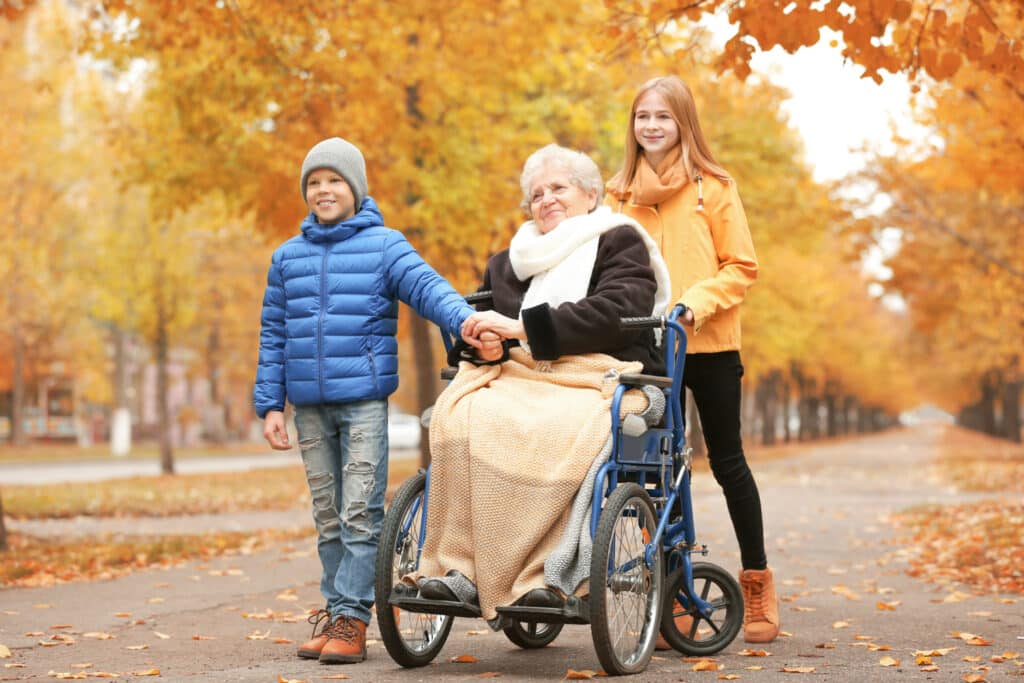 grandma in wheelchair walking with her two grandkids on autumn day