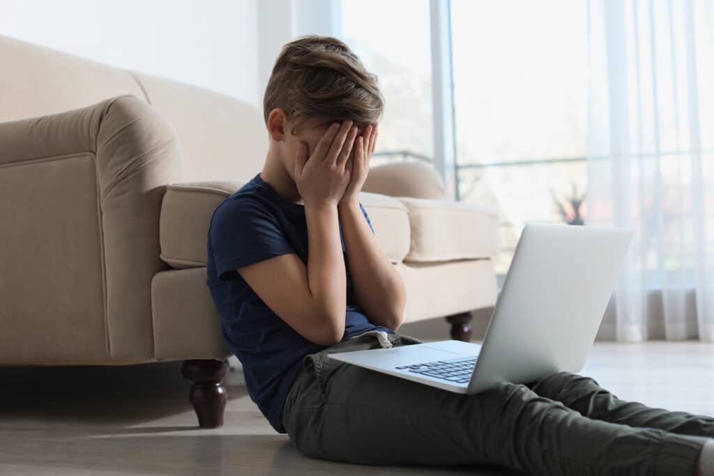child covering eyes in front of a laptop