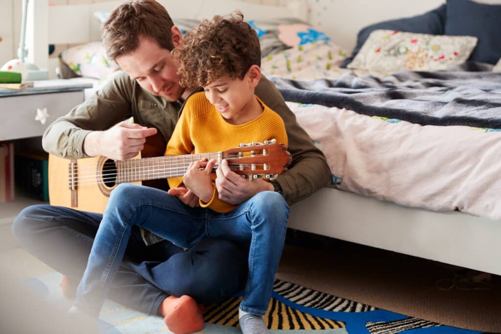 Father teaching his little boy how to play guitar