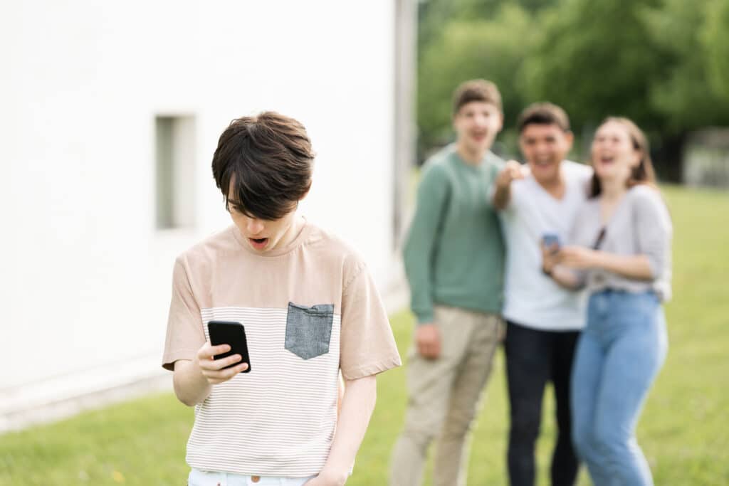 kid in shock looking at his phone with three people laughing at him in background