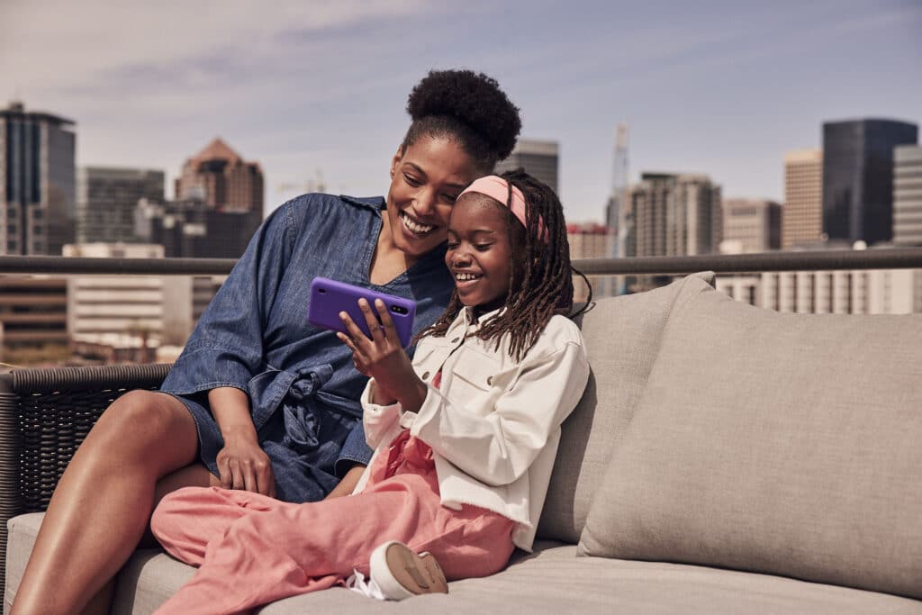 African American mom and daughter smiling and taking a selfie together on a rooftop with a city skyline in the background