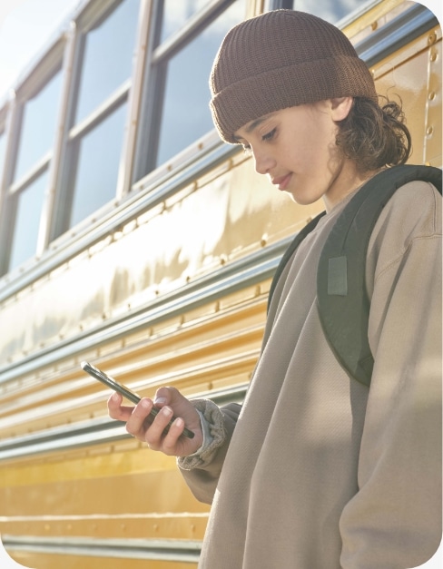 Teen boy looking at cell phone for kids outside school bus