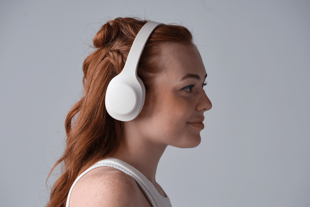 Teen with white earphones on listening to music against a grey background.
