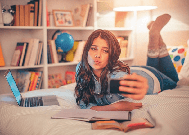girl laying on bed doing homework and taking a selfie with her Gabb cell phone for kids